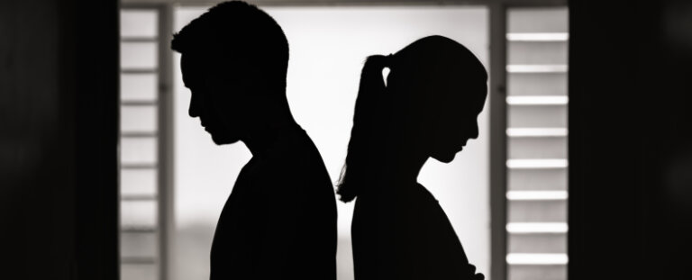 a silhouette of a man and a woman in an argument back to back in front of a window