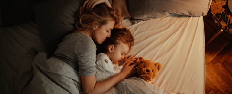 mother and daughter laying bed together with a stuffed bear